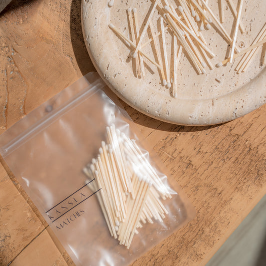 a pack of white matches in a clear kansla branded bag. there are also loose matches next to this on a travertine dispay tray