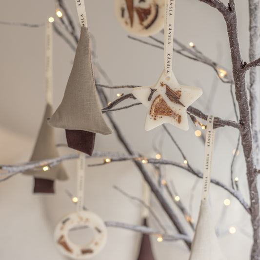 A close up of 2 linen christmas tree decorations styled with soy wax christmas tree decorations in a star and circle shape