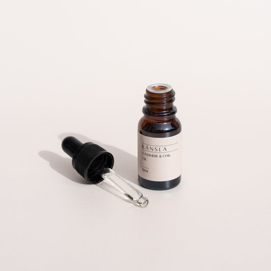 A small amber glass jar with a black dropper containing a scent oil, labelled Känsla with a white background. the lid has been removed to show the glass dropper