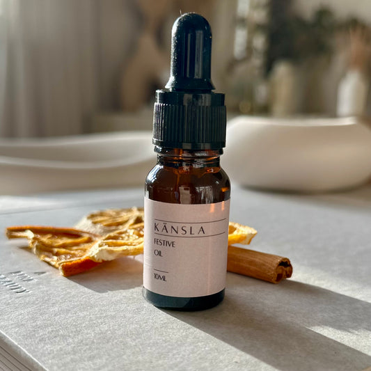 a close up of the kansla festive orange oil scent. there are decorative orange and cinnamon slices next to the bottle of oil with a blurred background