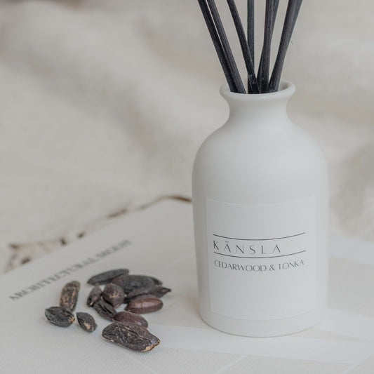 Close up of Cedarwood and tonka reed diffuser in white ceramic bottle with white label and black rattan reeds