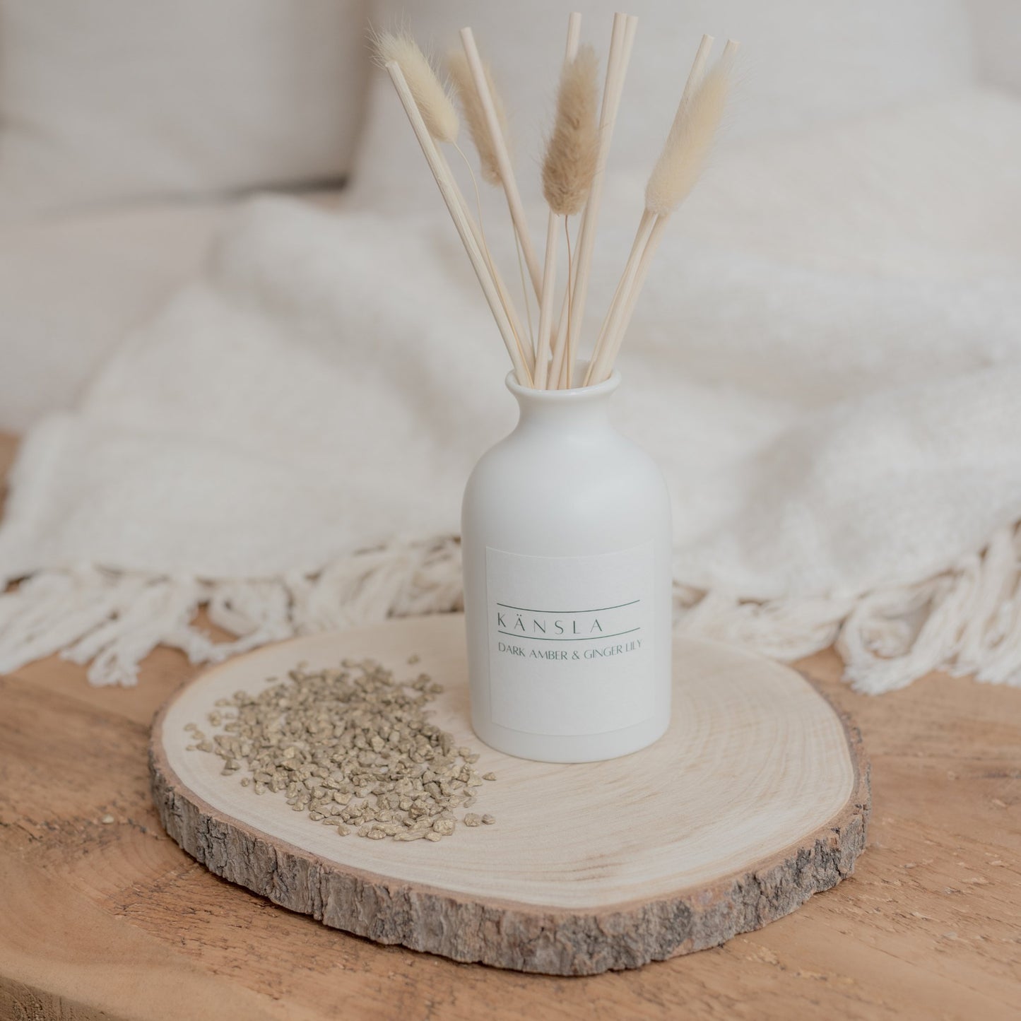 White ceramic reed diffuser with decorative dried bunny tail and rattan reeds white kansla label dark amber and ginger lily scent