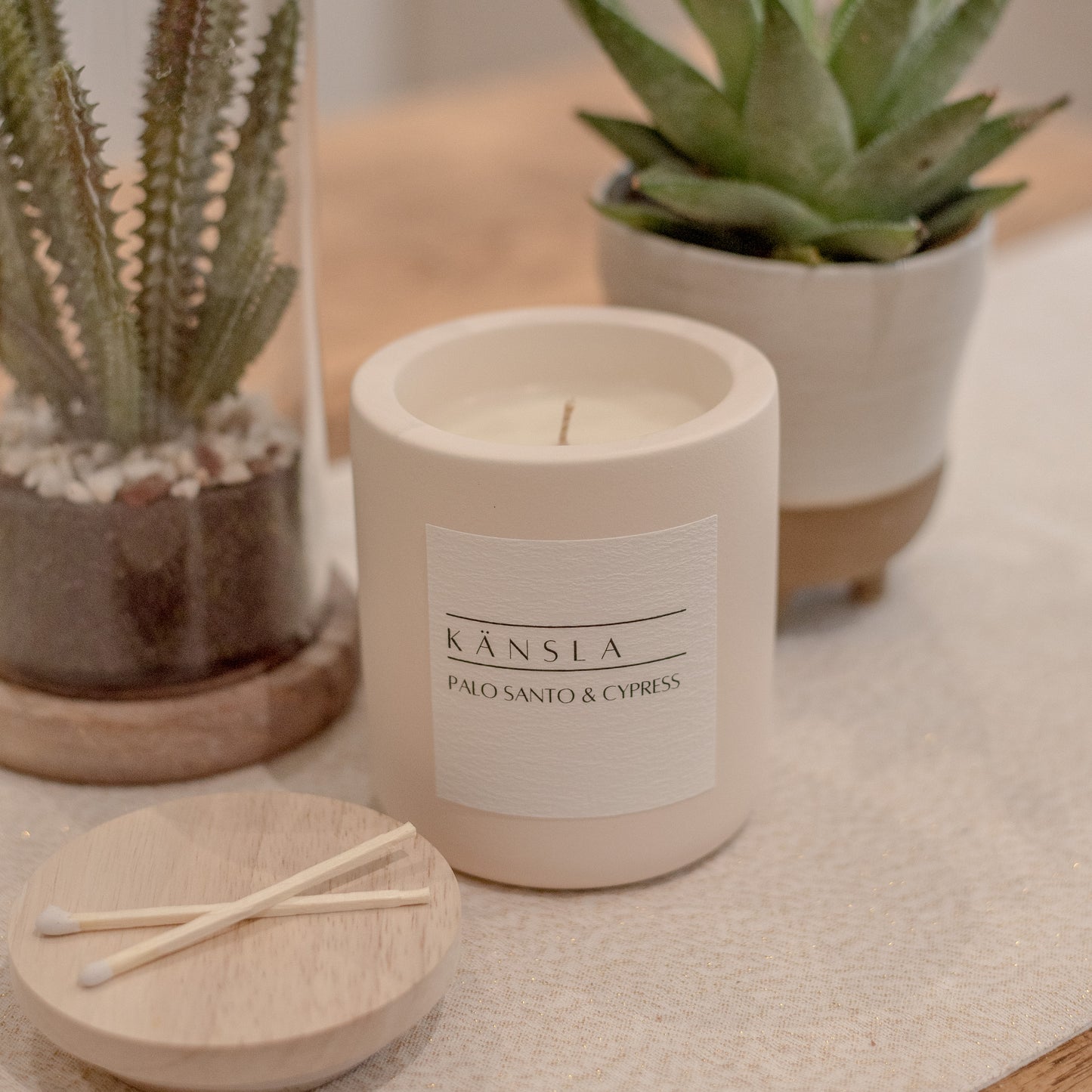 a close up of the concrete candle in palo santo and cypress scent. in the background there are two decorative vases