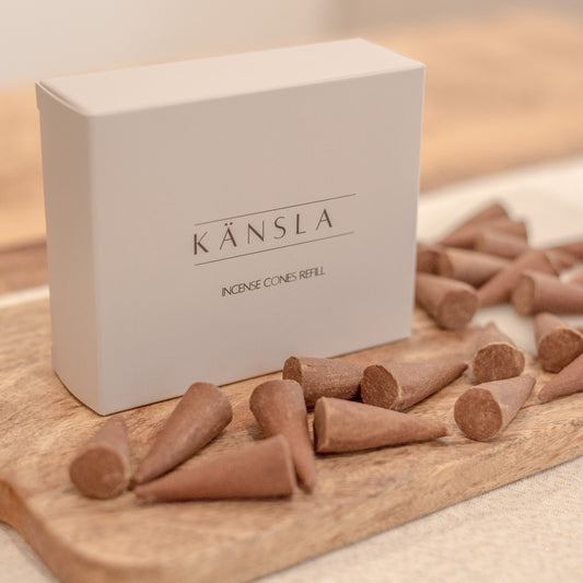 A box labelled Känsla Incense Cones Refill with multiple brown incense cones scattered in front of it on a wooden surface.