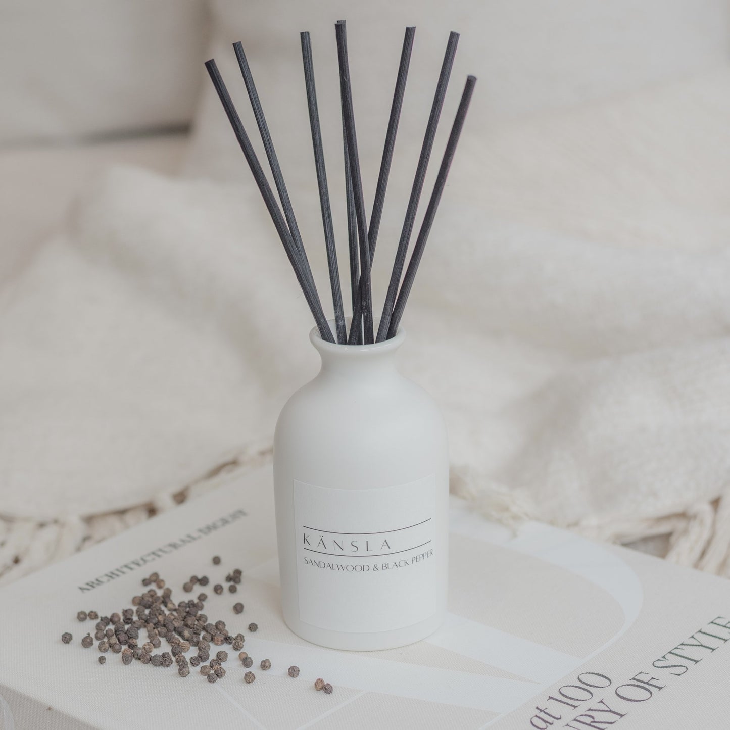 White ceramic reed diffuser with black rattan reeds and white label sandalwood and black pepper