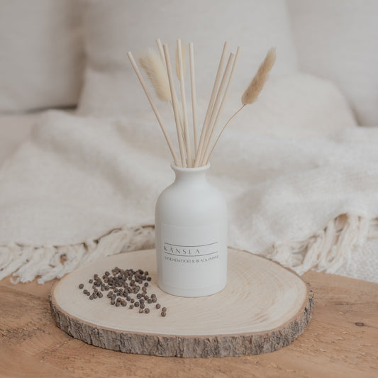 white ceramic reed diffuser with natural rattan reeds and decorative dried bunny tails on wooden plate