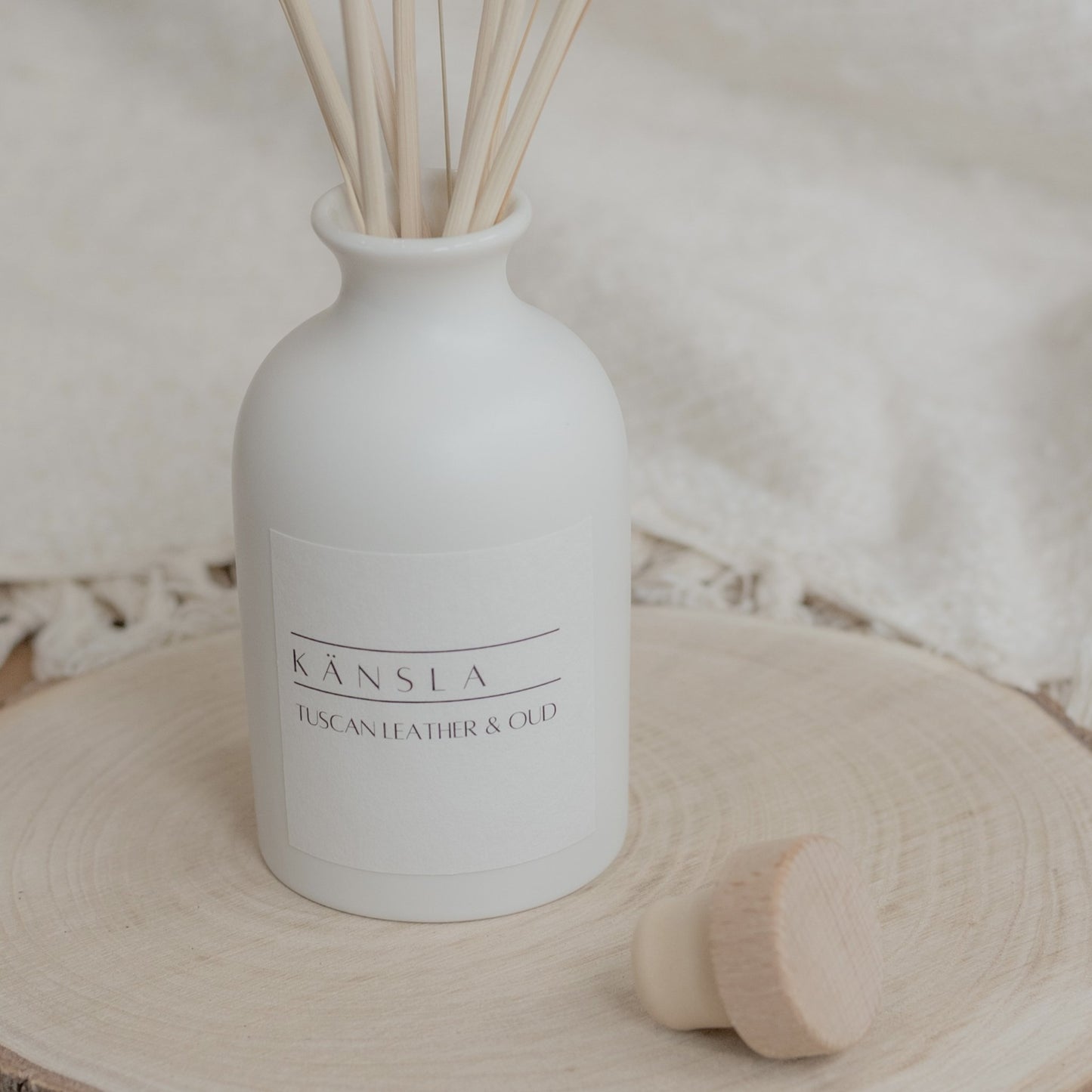 close up of white ceramic reed diffuser with natural reeds tuscan leather and oud