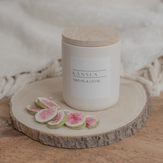 An image of a concrete candle jar with a wooden lid. There is a white label on the front of the candle that says kansla wild fig and cedar. There are dried decorative figs around the outside of the candle.