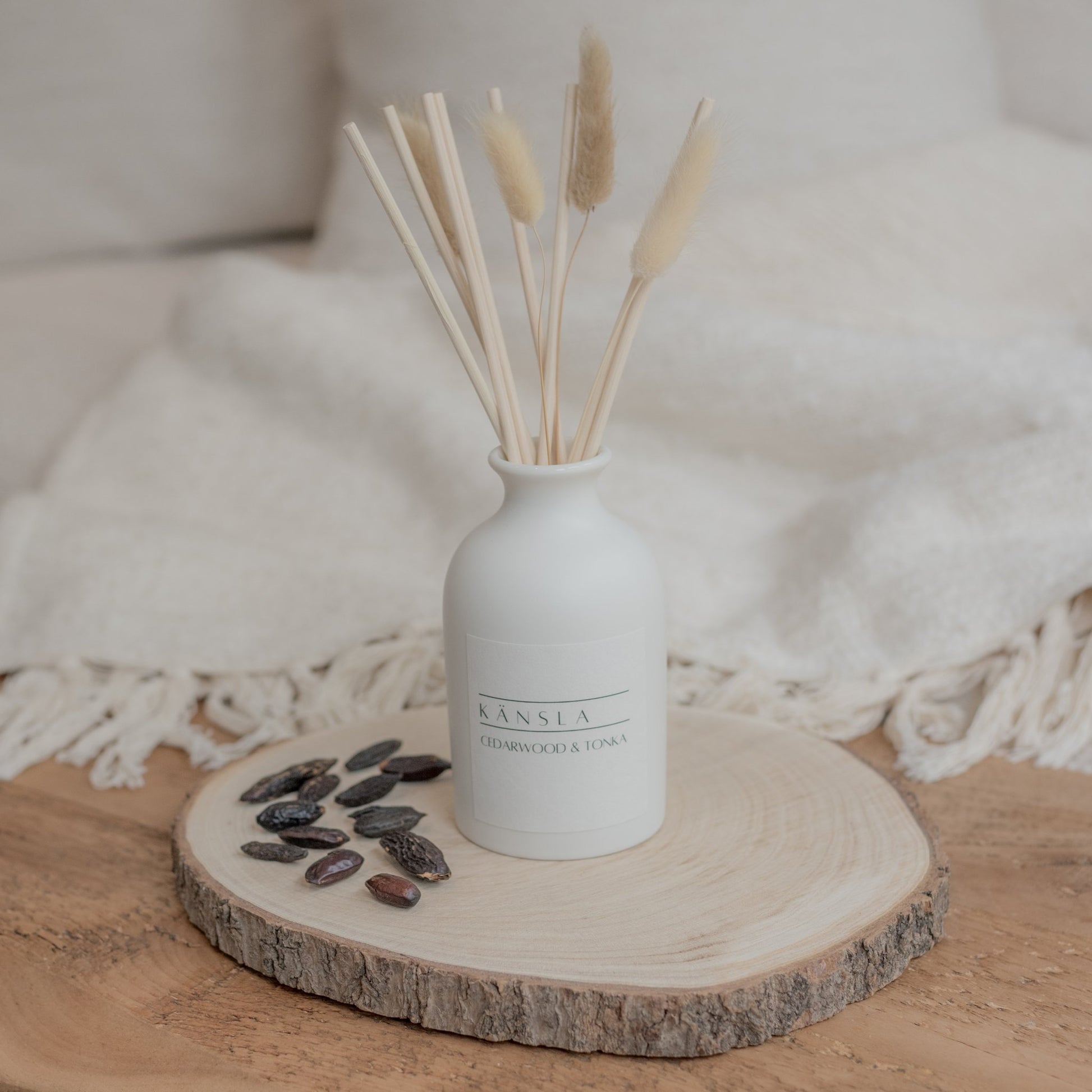 White ceramic reed diffuser with natural rattan reeds and decorative dried bunny tails and white label kansla cedarwood and tonka