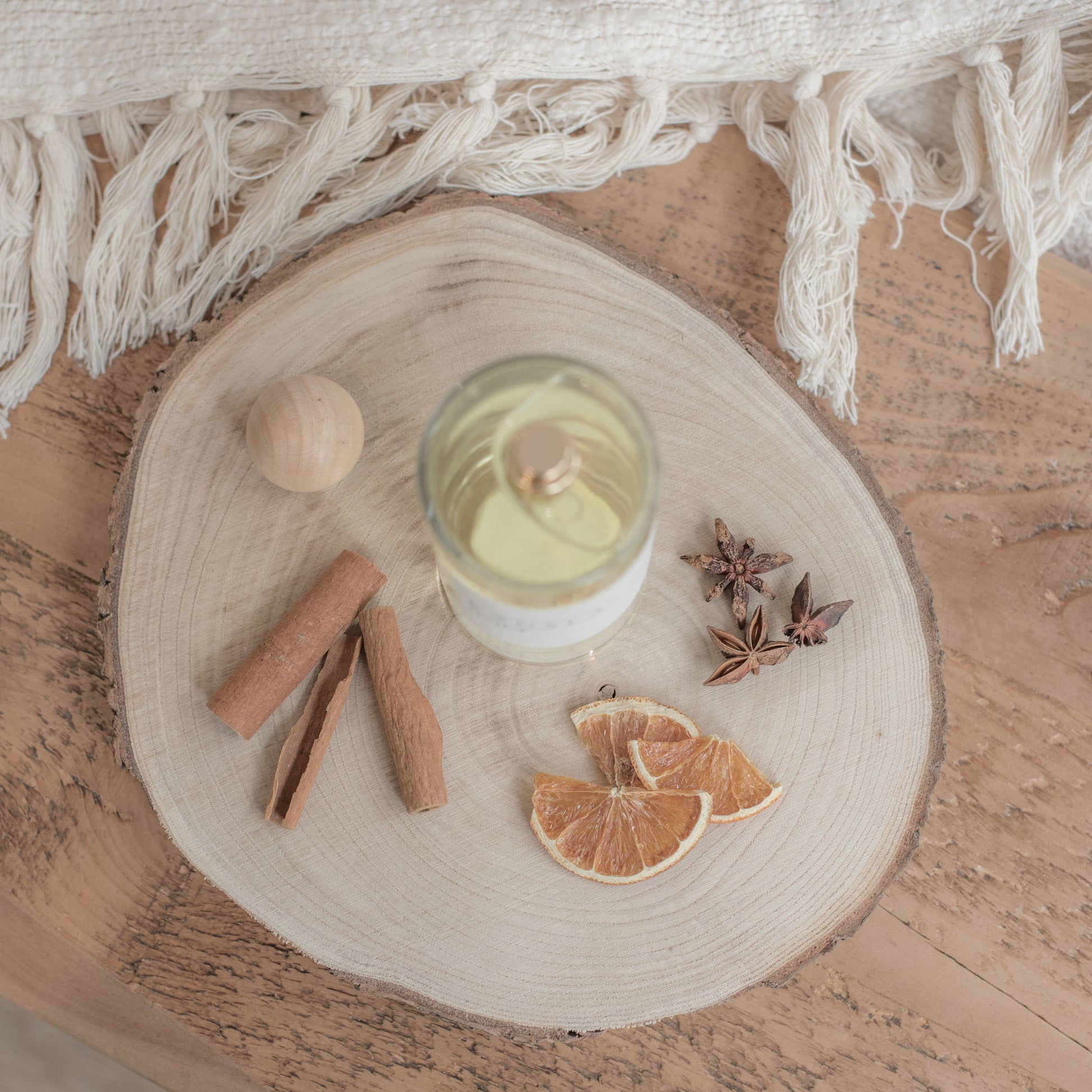 A picture taken from birds eye view of a clear glass bottle with a gold spray pump. The room spray is festive scent with dried orange and cinnamon decorations on a wooden tray 