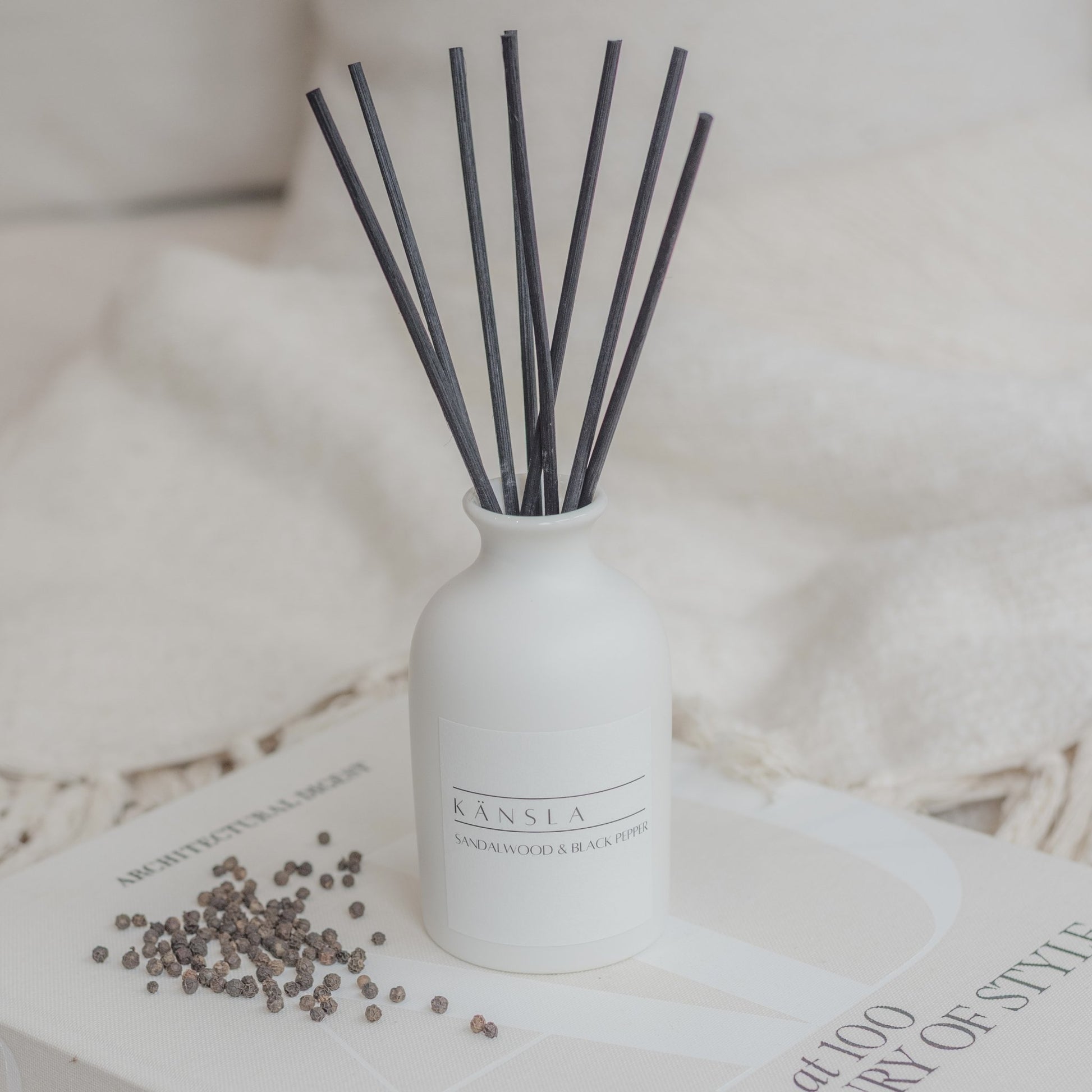 White ceramic reed diffuser with black rattan reeds and white label sandalwood and black pepper