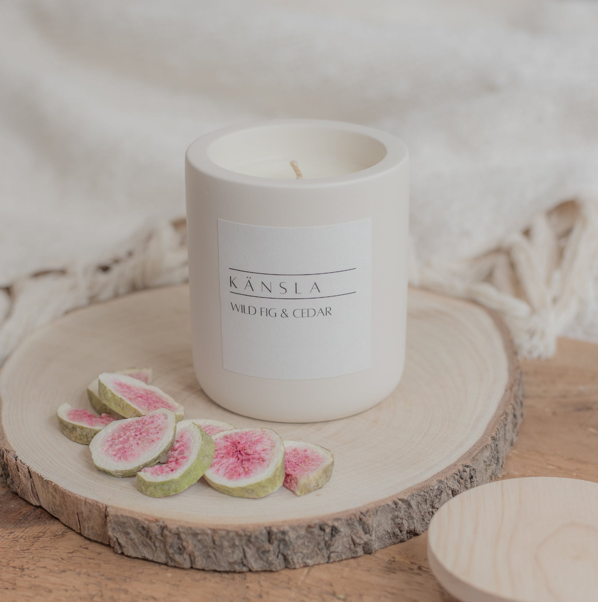 A concrete candle with a wooden lid off to the side. Placed on a wooden block with decorative figs around the outside 